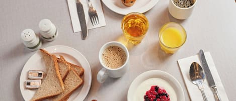 Une table de petit-déjeuner avec des croissants, du café, du jus de fruits, des toasts et un bol de fruits rouges.