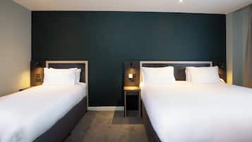 Habitación de hotel con dos camas, paredes verde oscuro y una mesita de noche pequeña con lámpara.
