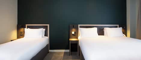 Ein Hotelzimmer mit zwei Betten, dunkelgrünen Wänden und einem kleinen Nachttisch mit einer Lampe.