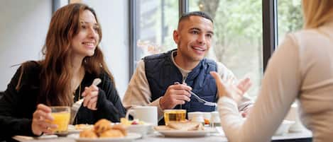 Tres personas comiendo en una mesa con alimentos para el desayuno, vistas al exterior y un interior moderno.