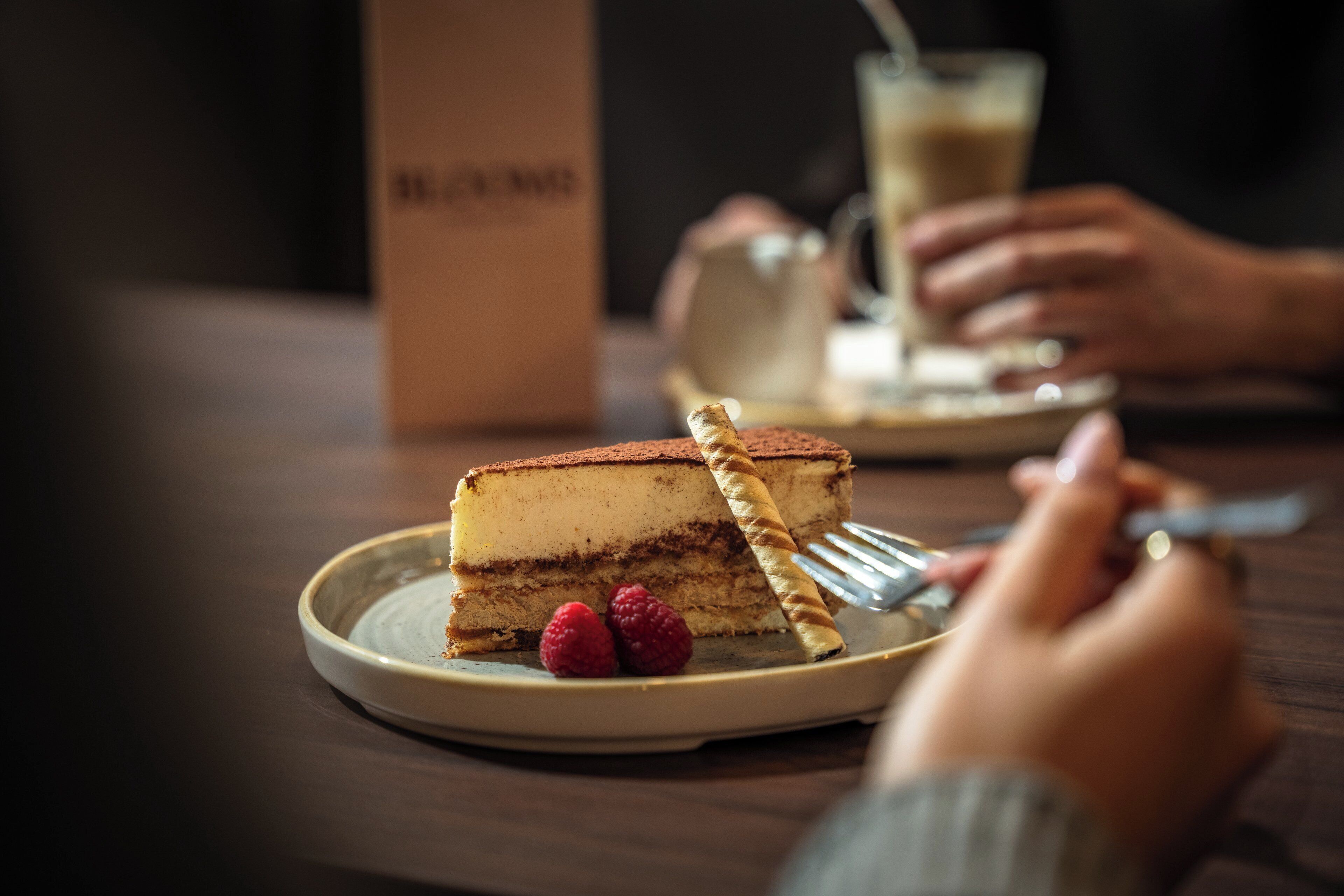Une part de gâteau à plusieurs couches, présentée sur une assiette avec une fourchette, et accompagnée de deux framboises.