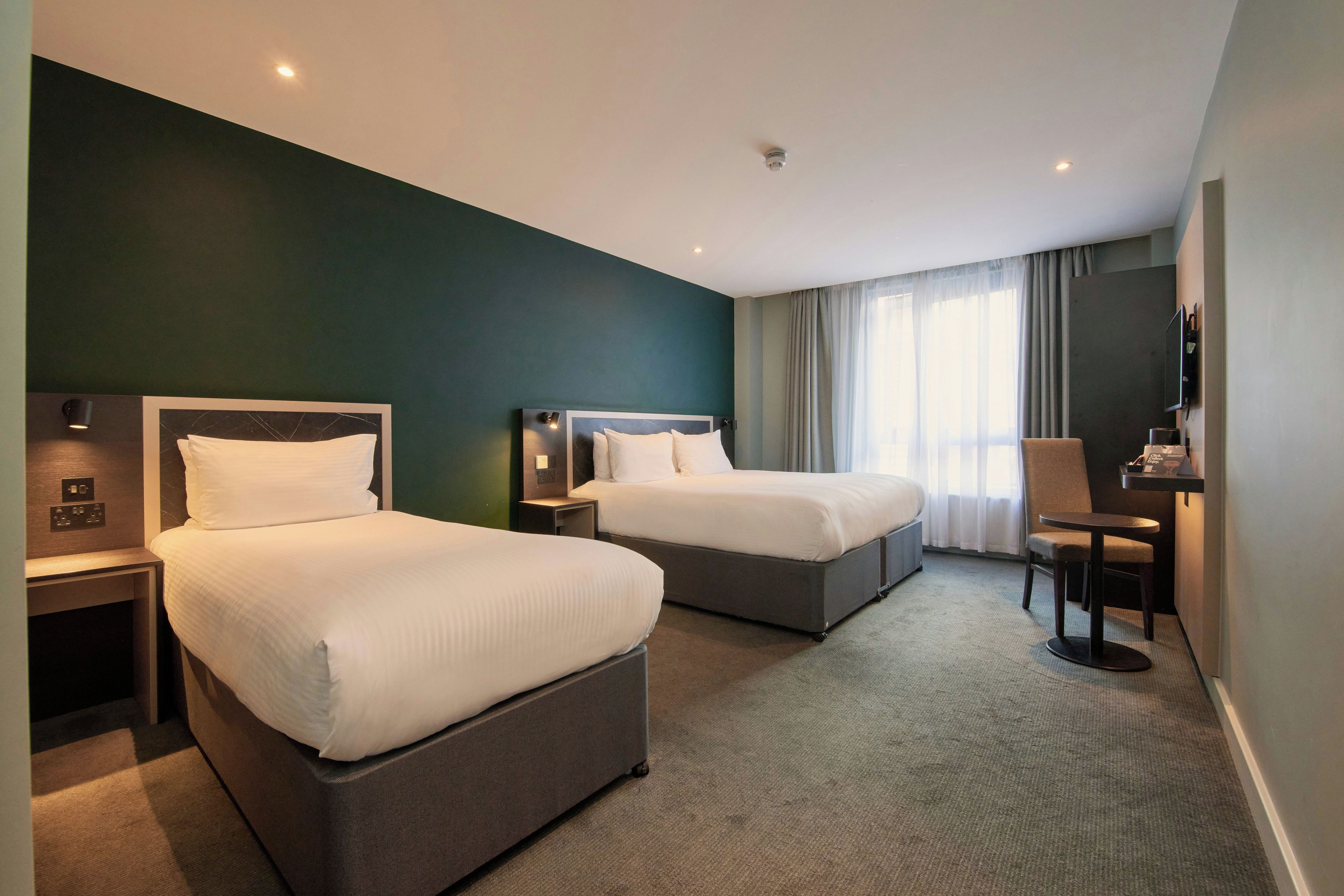 Ein Hotelzimmer mit zwei Betten, einem Schreibtisch, einem Sessel und einem Fernseher.