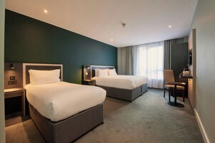 Ein Hotelzimmer mit zwei Betten, einem Schreibtisch, einem Sessel und einem Fernseher.