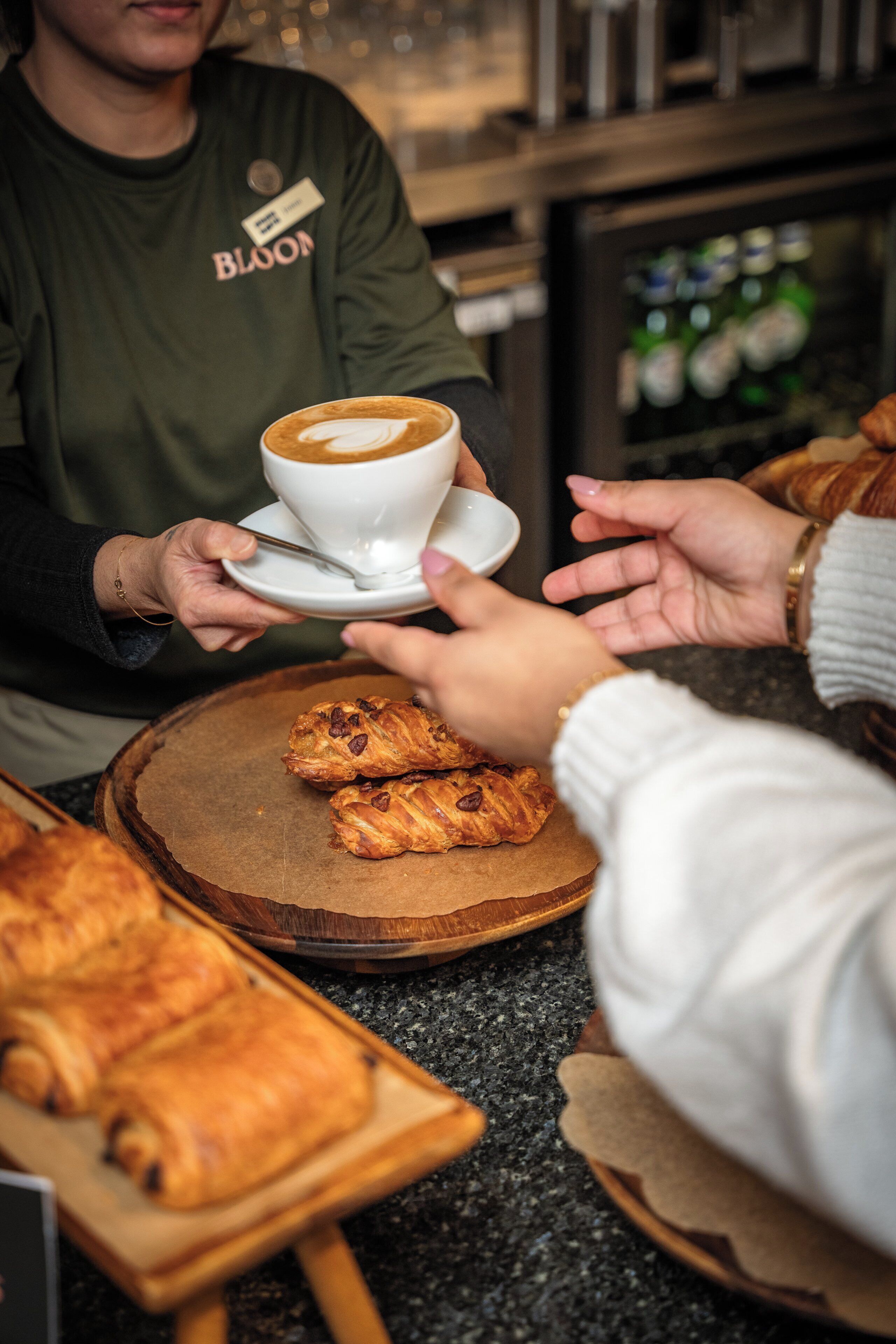 Une personne tient une tasse de café et une pâtisserie, tandis qu’une autre personne tend la main pour la prendre.