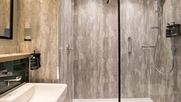 Een moderne badkamer met een douche met glazen wand, een witte wastafel en een muur met een marmerstructuur.