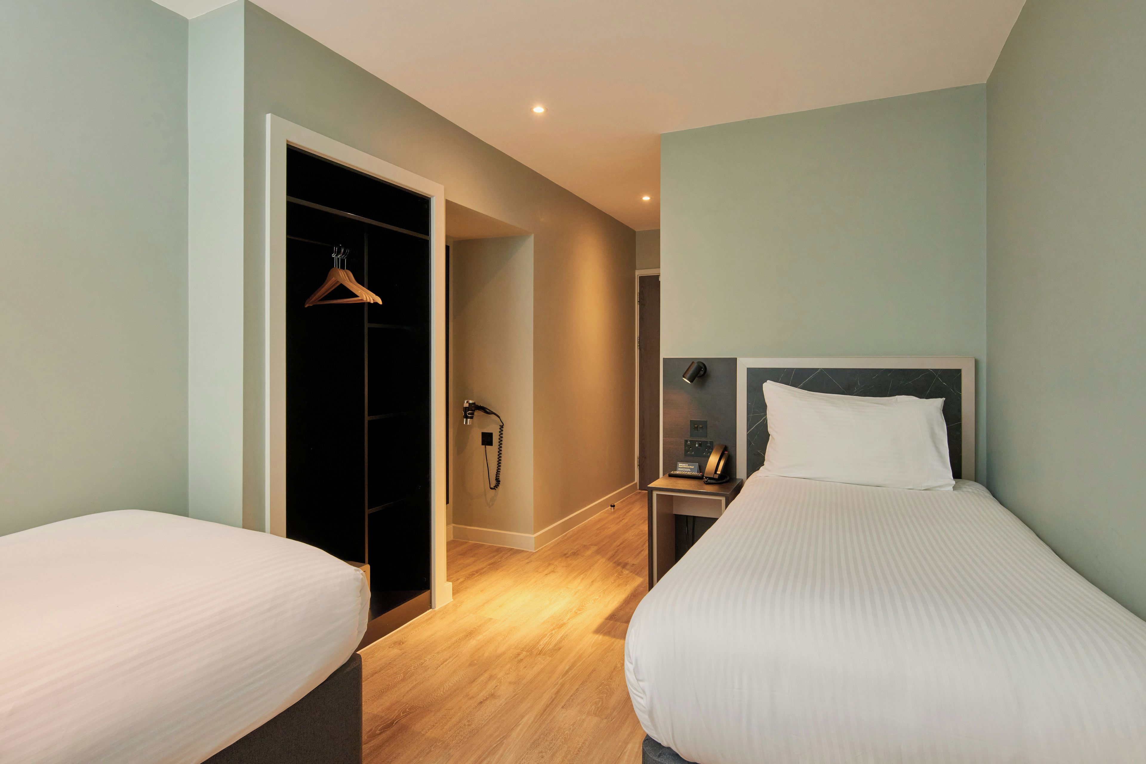 Une chambre d’hôtel avec deux lits, une armoire, une table de chevet avec une lampe et un téléphone.