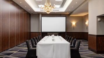 Una sala conferenze con un lungo tavolo, sedie nere, uno schermo per proiettore e un lampadario.