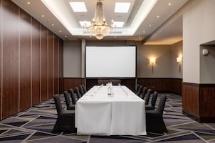 Una sala conferenze con un lungo tavolo, sedie nere, uno schermo per proiettore e un lampadario.