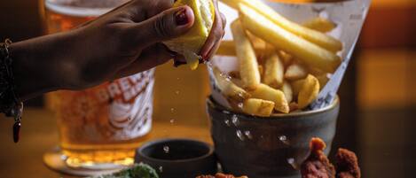 A plate with fried chicken, fries, and salad, a glass of beer, and a hand squeezing a lemon over the fries.