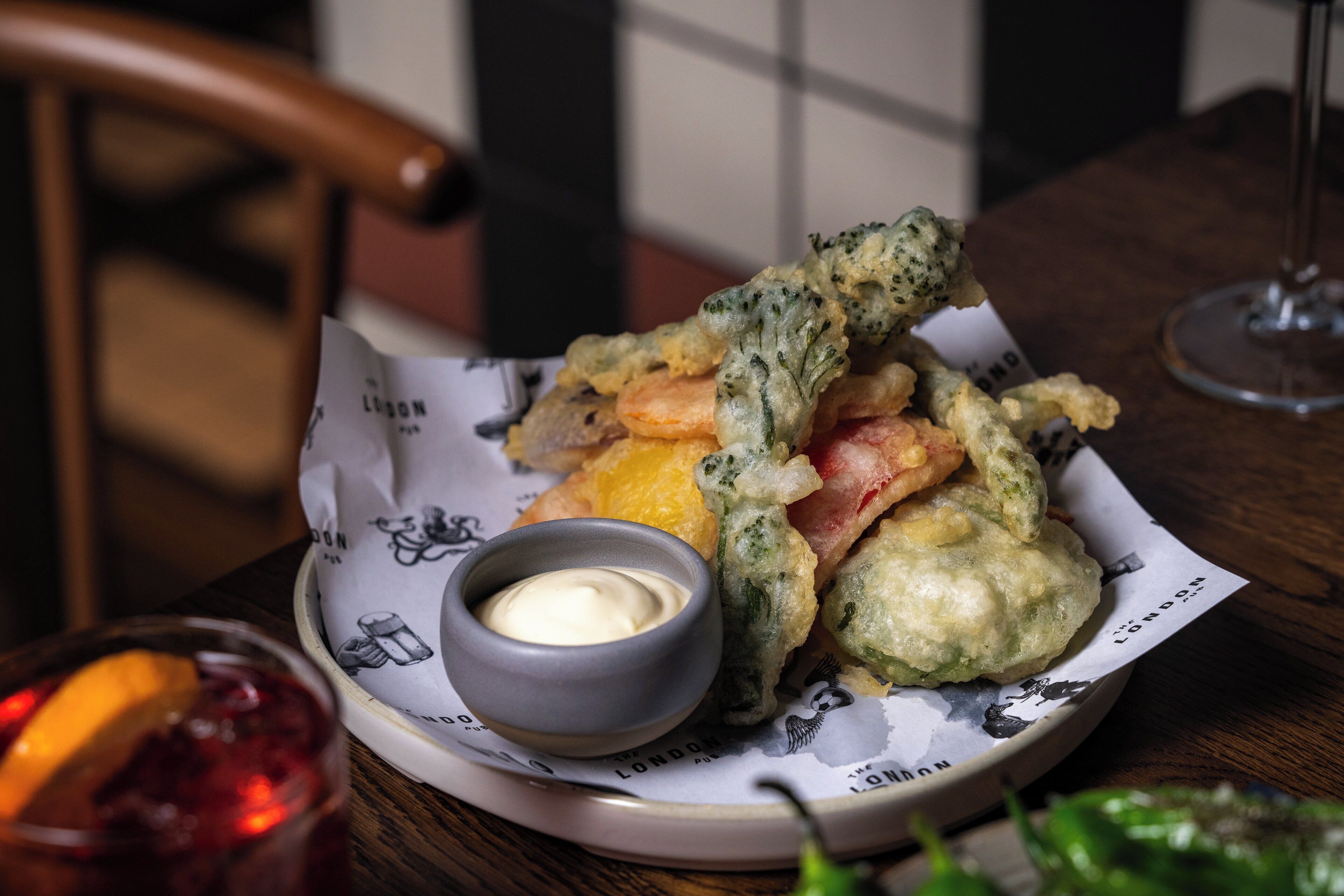 A plate of fried food with dipping sauce and a glass of red drink on a wooden table.
