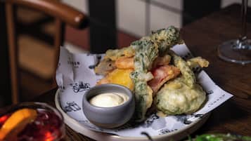 A plate of fried food with dipping sauce and a glass of red drink on a wooden table.