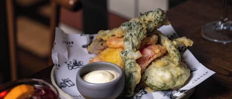 A plate of fried food with dipping sauce and a glass of red drink on a wooden table.