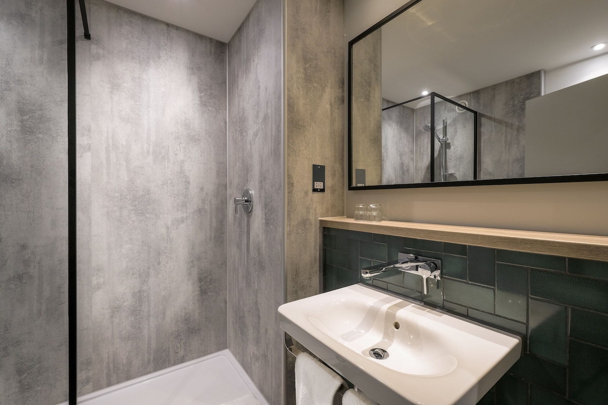 A modern bathroom with a large mirror, a white sink, and a shower area.