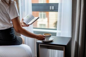 A person reading a book next to a cup of coffee on a small table by a window.