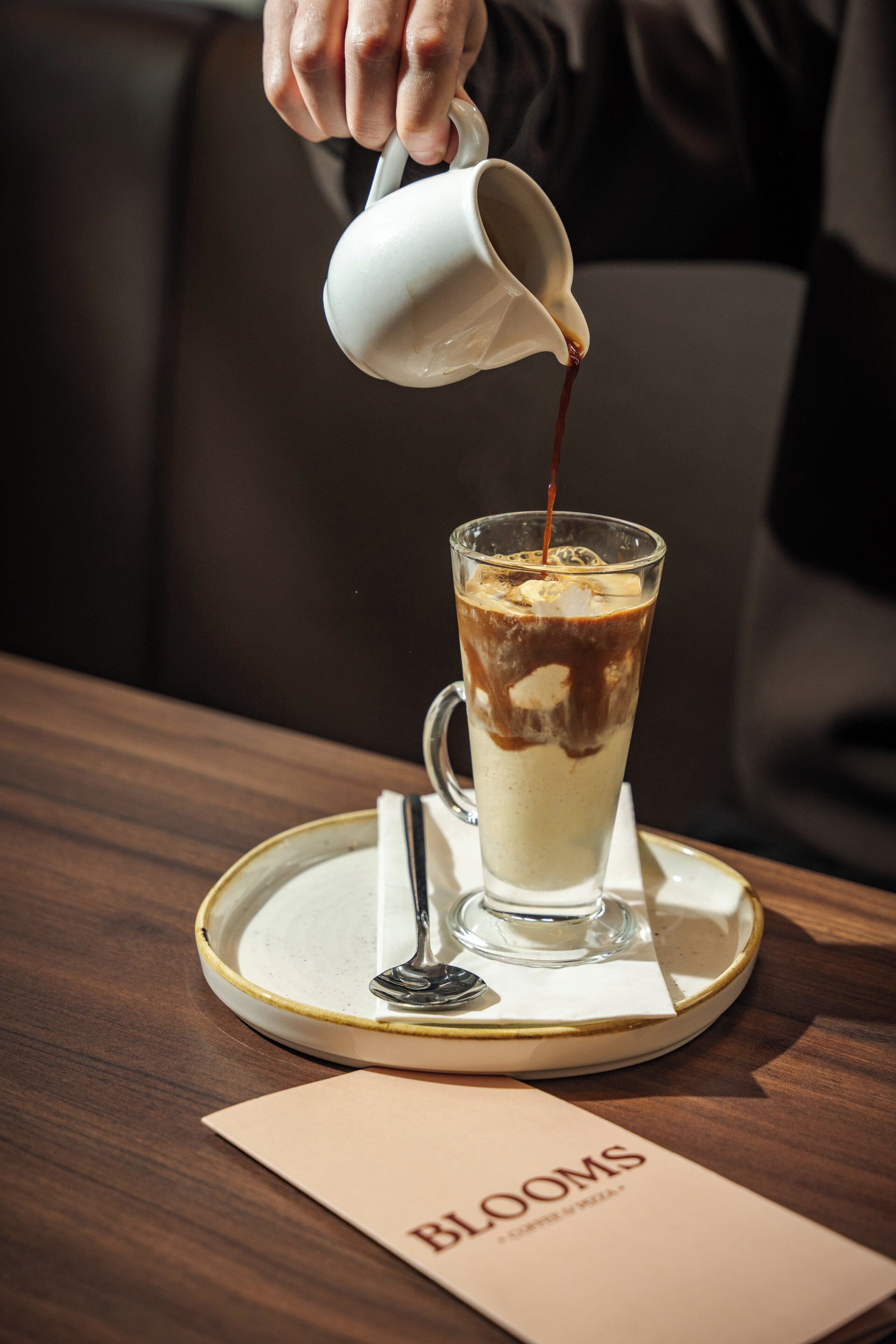 A person pouring a drink into a tall glass on a tray.