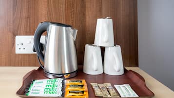 A tray with a kettle, coffee cups, and milk packets on a wooden table.