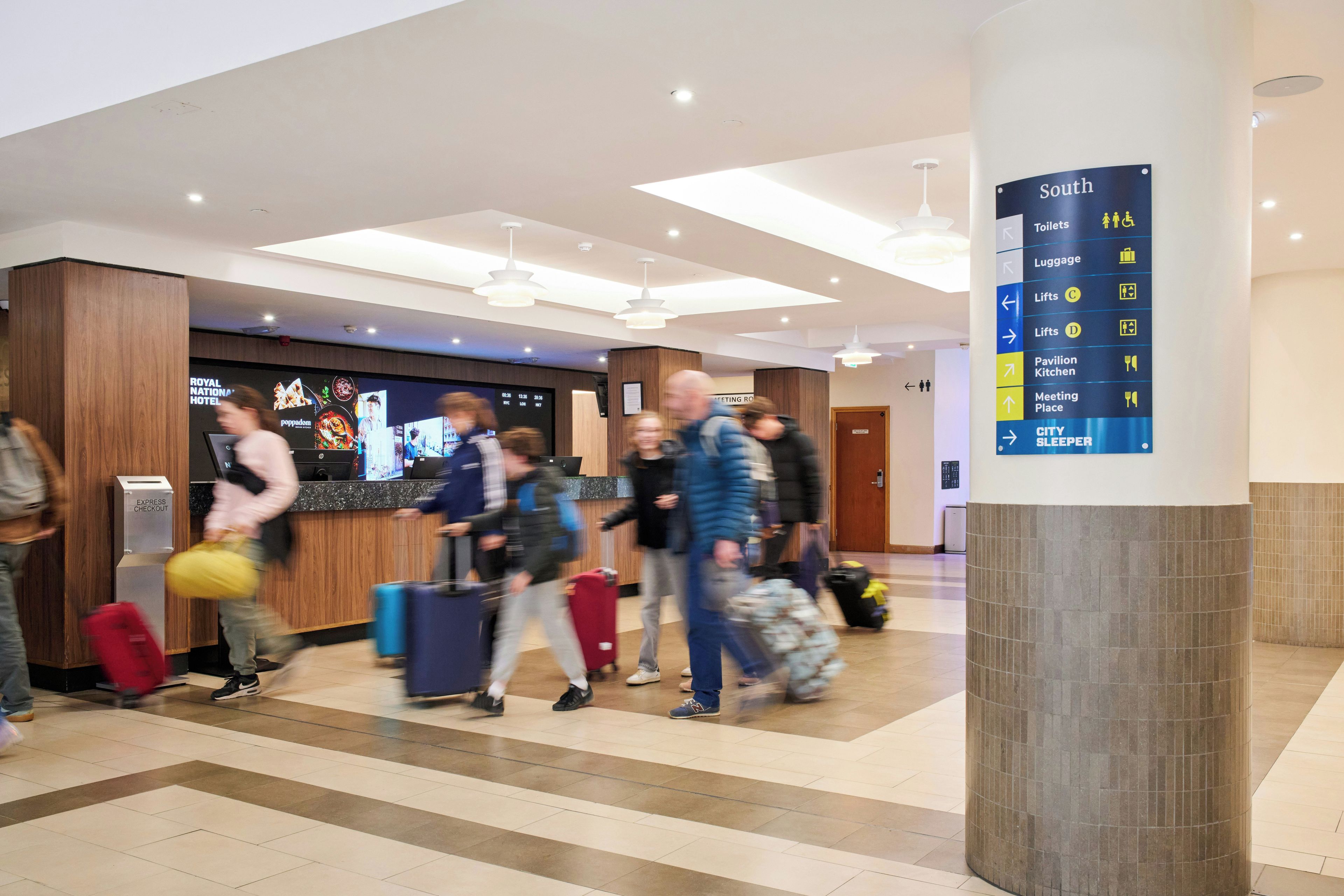 A hotel lobby with a directory sign indicating amenities such as toilets, luggage storage, and meeting places.