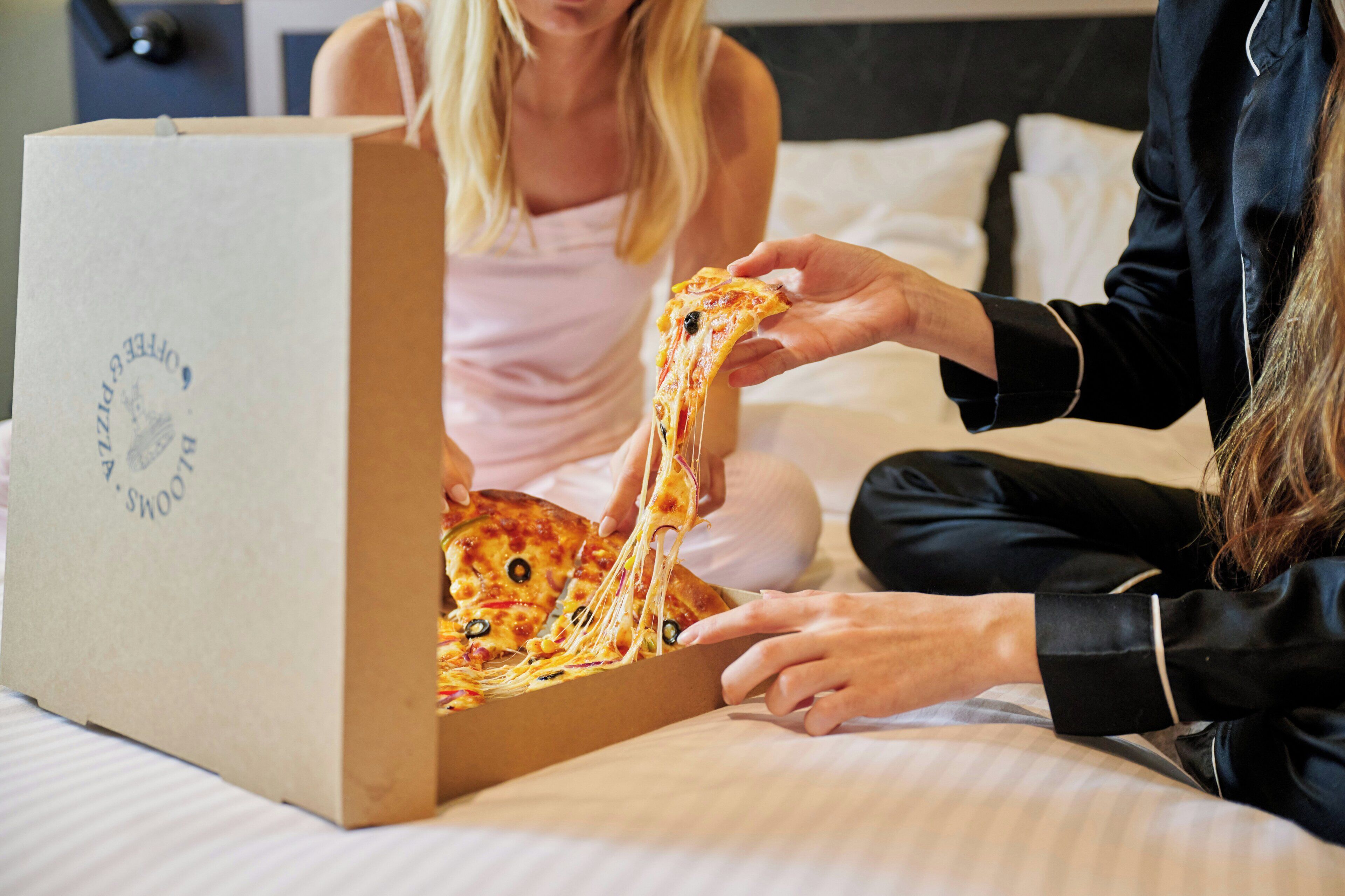 A person pulling a slice of pizza from a cardboard box on a bed.