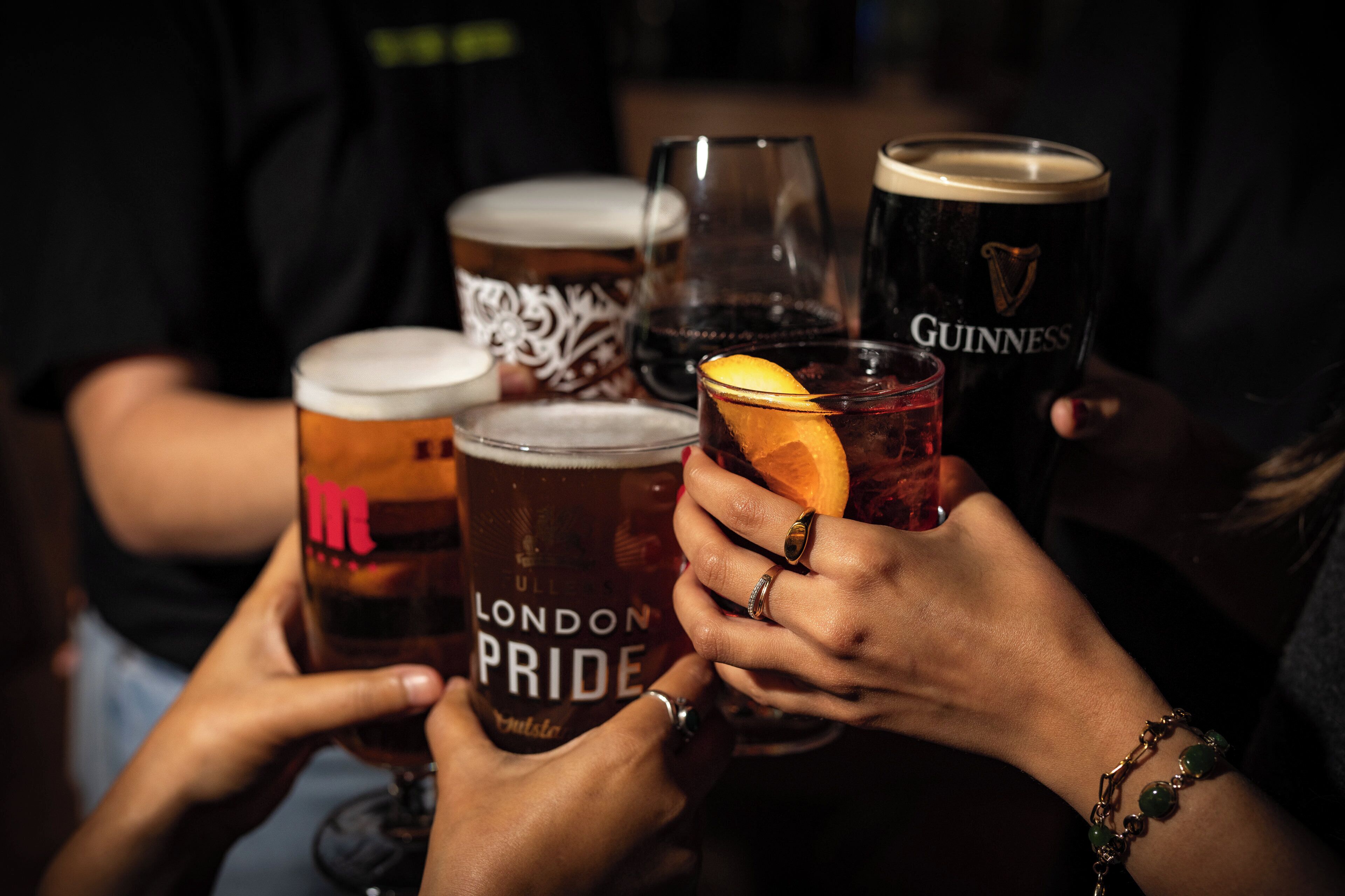 Un grupo de personas sosteniendo diferentes jarras de cerveza, incluyendo marcas como 'London Pride' y 'Guinness'.