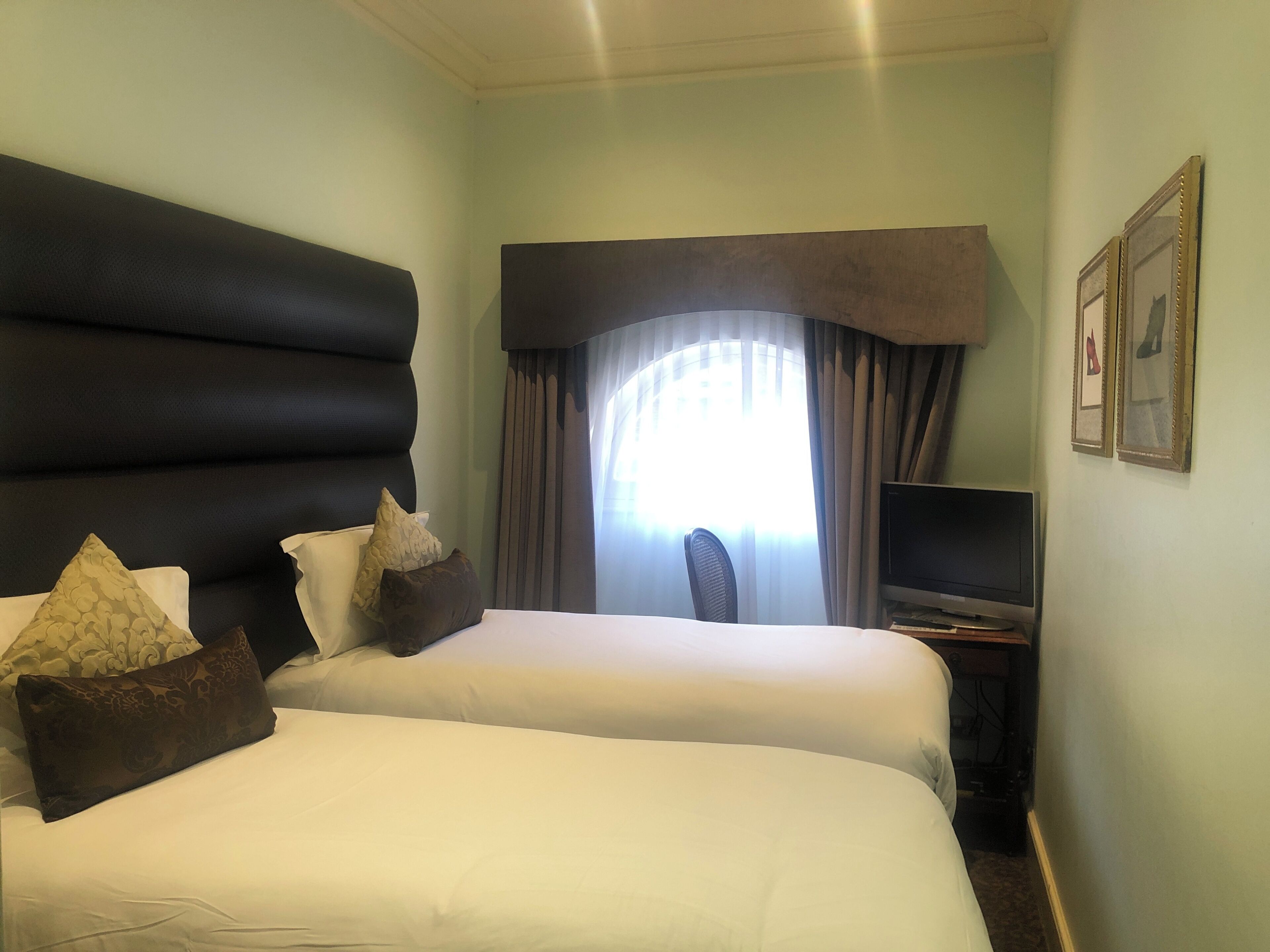 A hotel room with two beds, a desk with a computer, a chair, and a window with curtains.