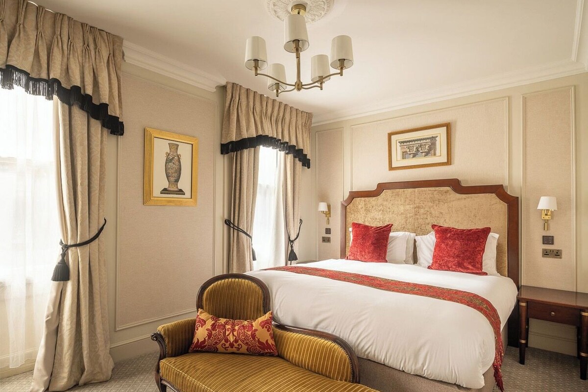 A hotel room with a large bed, a bench, a chandelier, and a painting on the wall.