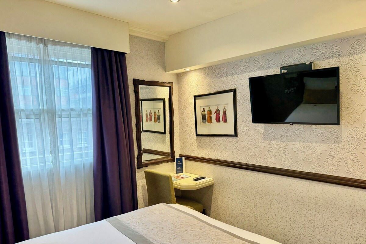 A hotel room with a bed, a vanity with a mirror, a framed picture, and a television.