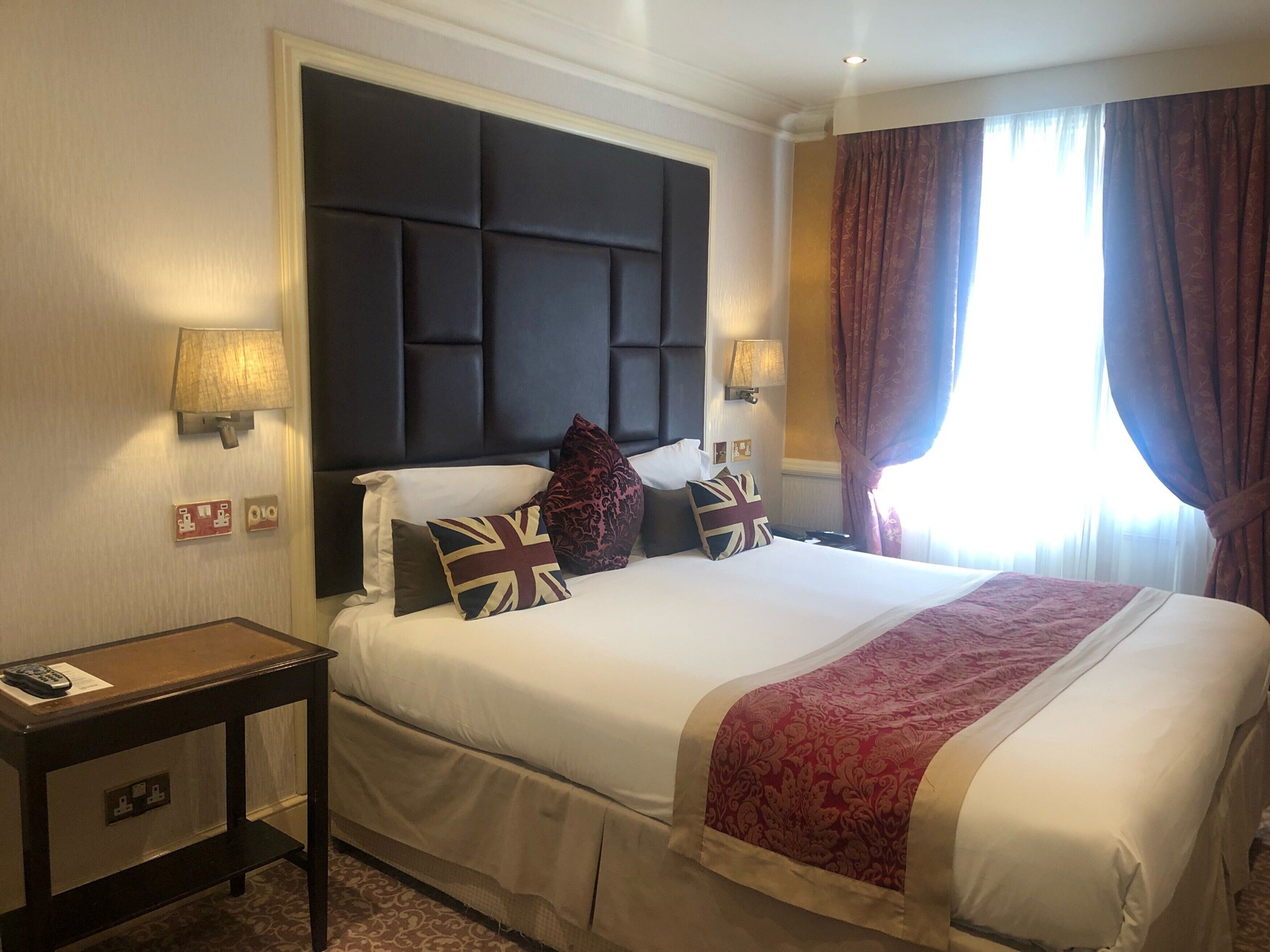 A hotel room with a large bed, two bedside lamps, a nightstand, and a window with curtains.