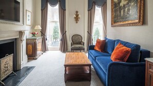 A spacious living room with a blue sofa, a wooden coffee table, a fireplace, and a large painting on the wall.