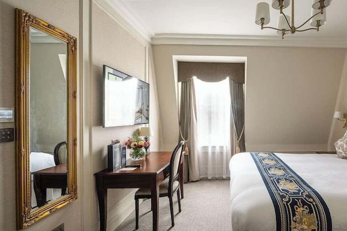 Une chambre d’hôtel avec un grand lit, un bureau avec une chaise, un miroir et un lustre.