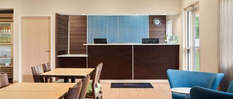A hotel lobby with a reception desk, seating area, and a clock on the wall.