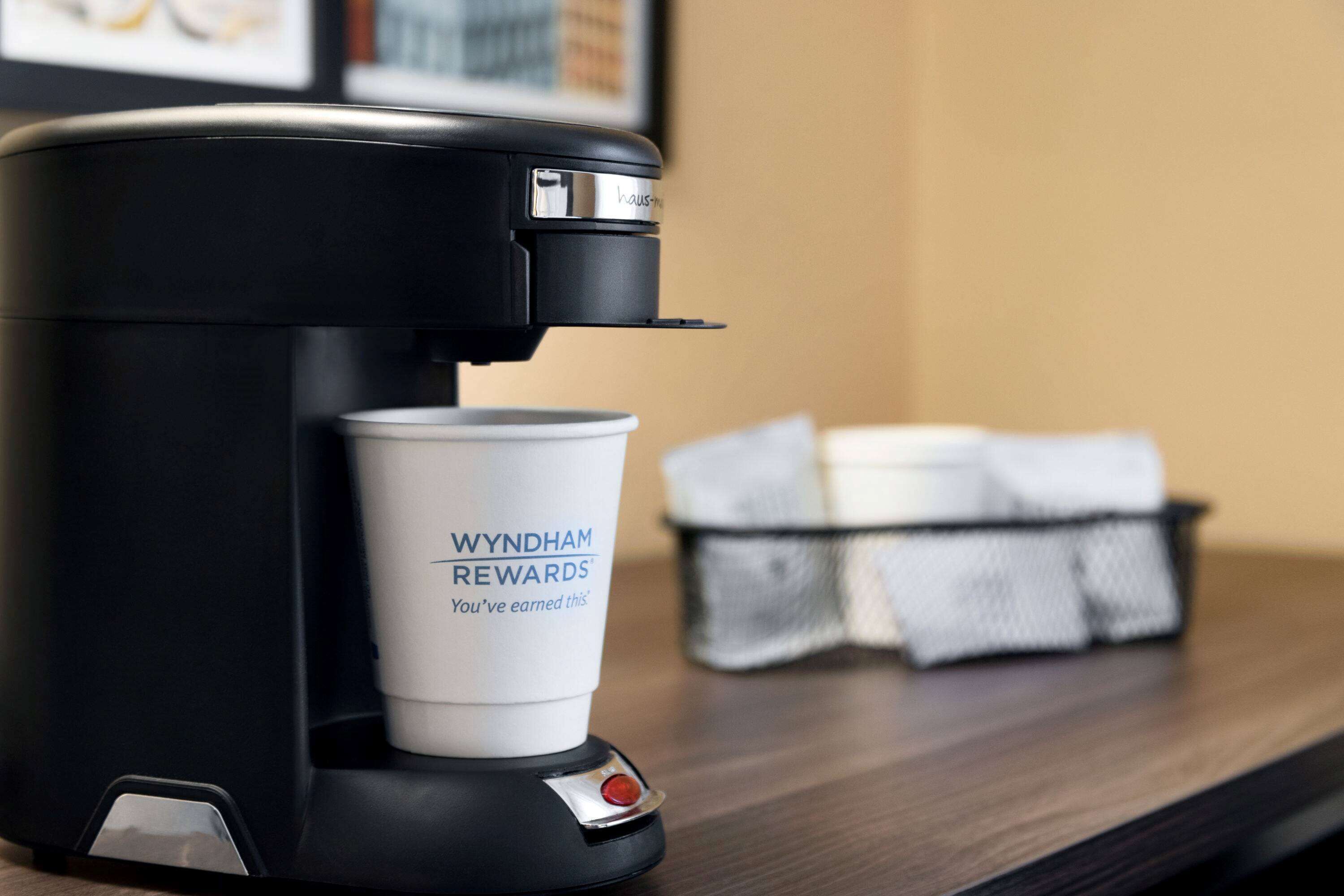 Une machine à café, avec une tasse portant l’inscription « WYNDHAM REWARDS », posée sur une surface en bois.