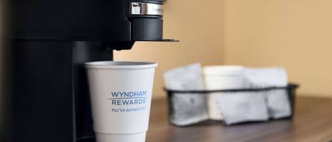 A coffee machine with a cup labeled "WYNDHAM REWARDS" on a wooden surface.