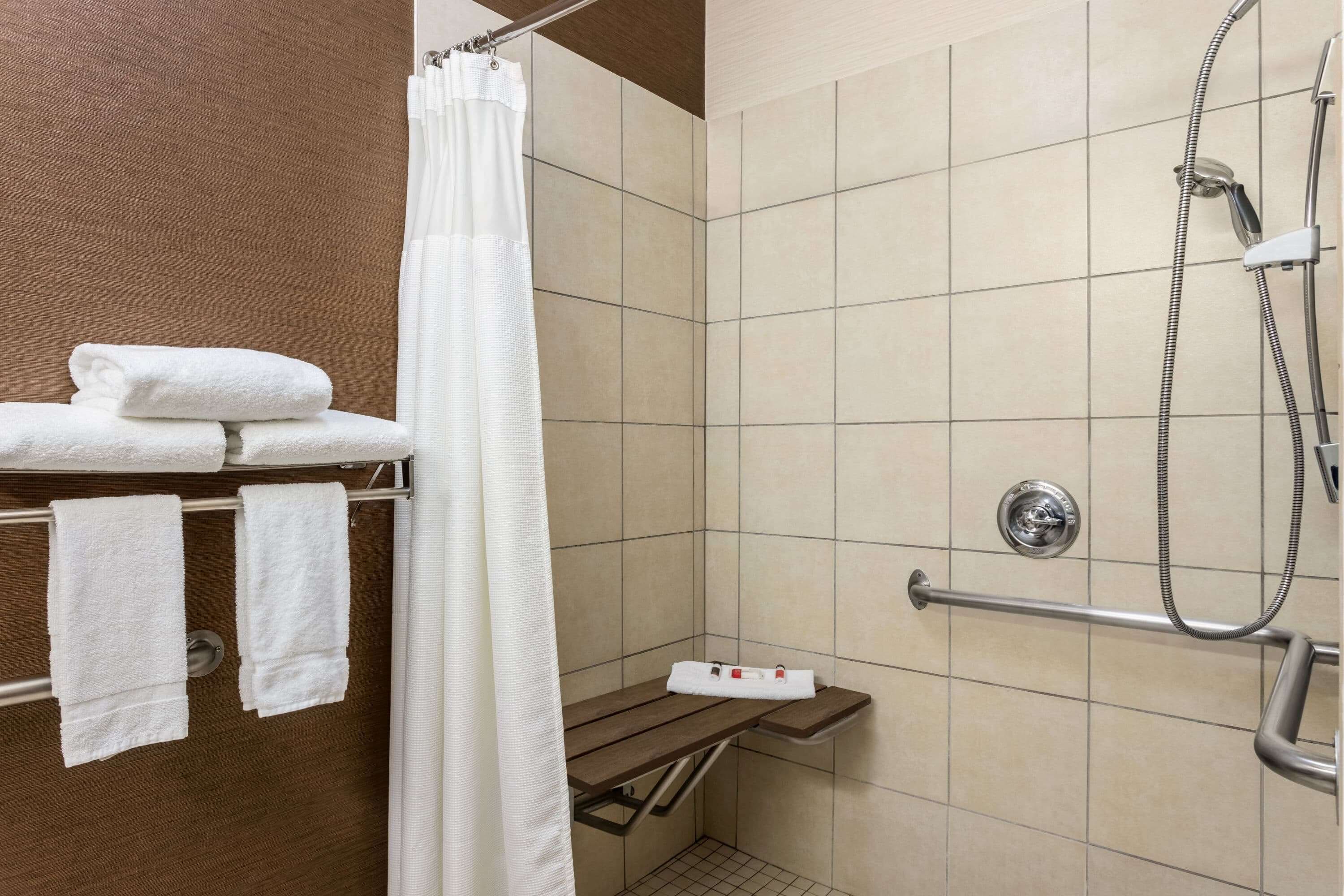 A shower area with a grab bar, a towel rack with folded towels, and a showerhead.
