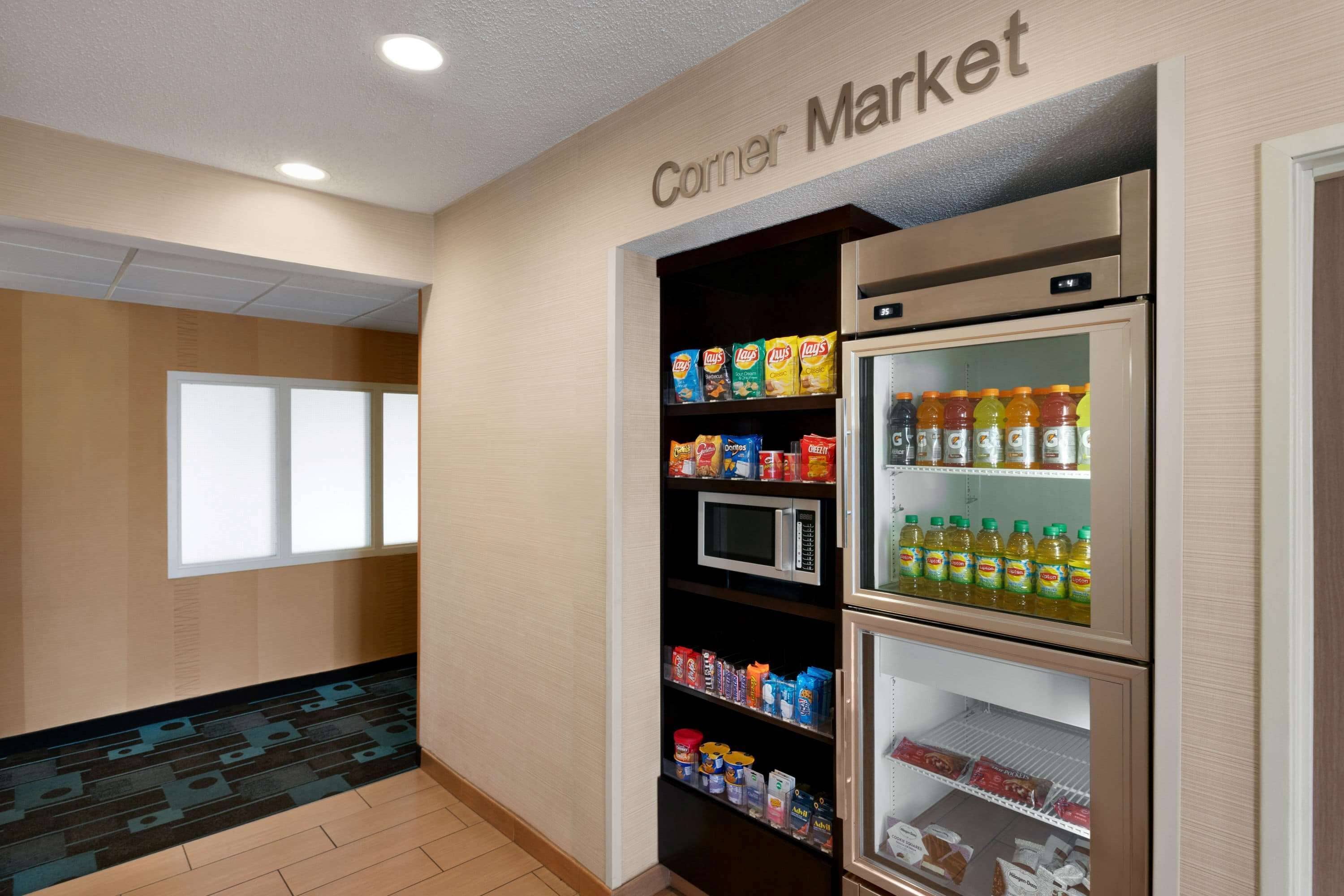 A corner market with shelves stocked with snacks, a microwave, and a refrigerator with beverages.