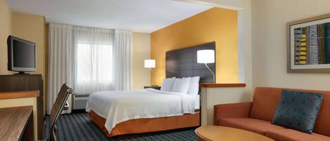 A hotel room with a bed, a sofa, a table, a TV, and a window with curtains.