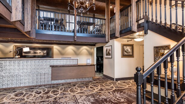 A spacious lobby with a high ceiling, a reception desk, and a staircase leading to an upper level. -  Holland America Skagway Inn (Skagway)
