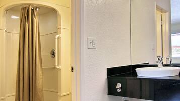 A modern bathroom with a curved shower, a black sink, and a large mirror.