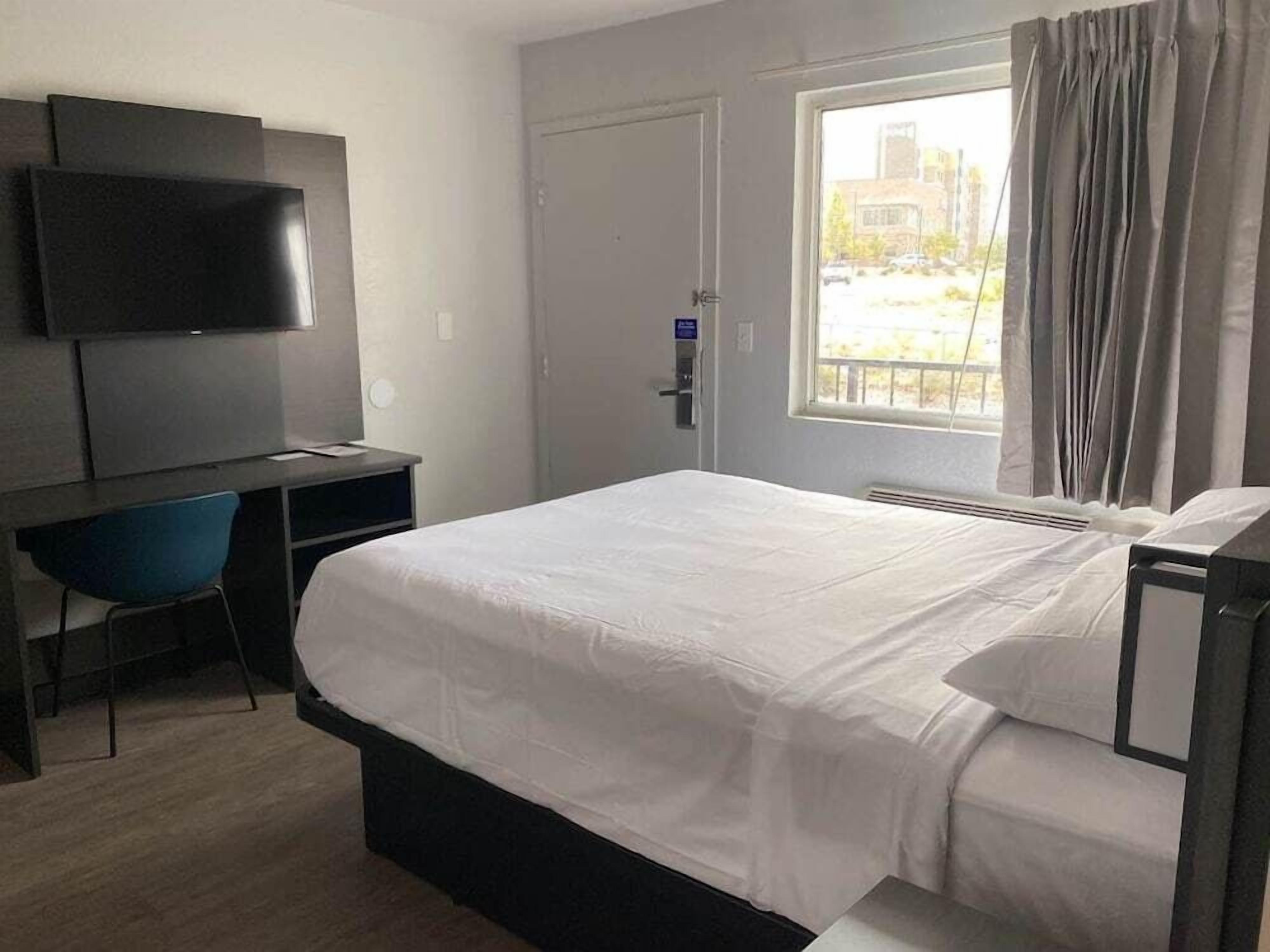 A hotel room with a bed, a desk with a chair, a television, and a window with curtains.