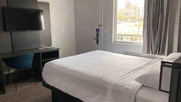 A hotel room with a bed, a desk with a chair, a television, and a window with curtains.