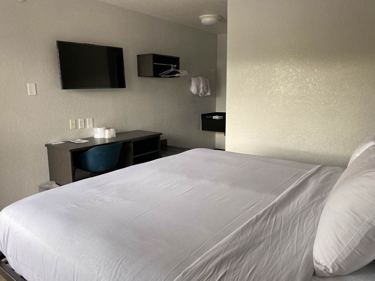 Habitación de hotel con una cama grande, un escritorio con silla, un televisor de pantalla plana en la pared y un mueble bajo.