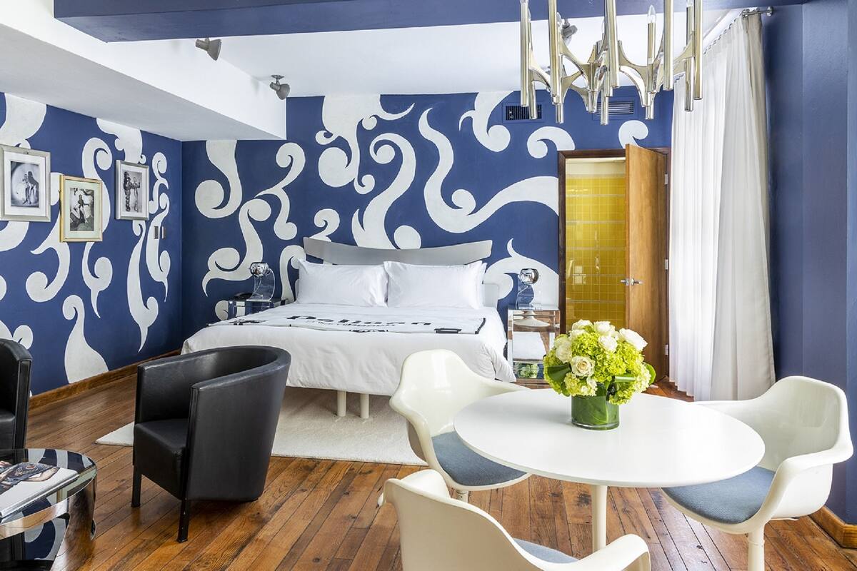 A bedroom with a bed, a white round table with chairs, a wardrobe, and a wall with a blue and white pattern.