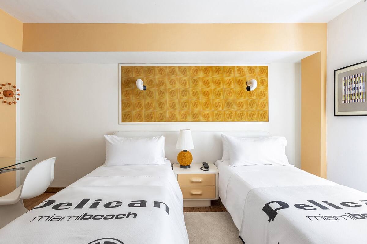 A hotel room with two beds, a nightstand, a lamp, and a wall art piece.