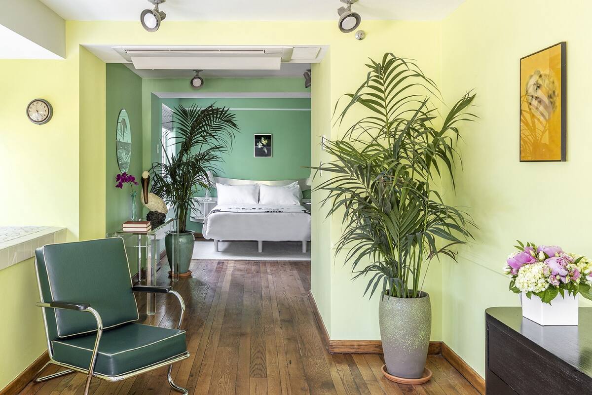 A hotel room with a bed, a chair, a potted plant, and a painting on the wall.