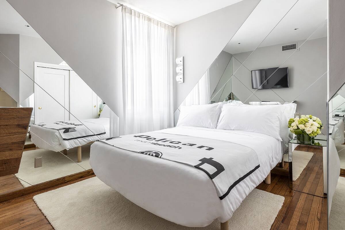 A modern hotel room with a large bed, a TV mounted on the wall, and a mirror reflecting the room.