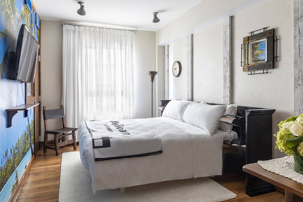 A neatly arranged bedroom with a bed, bedside table, lamp, and a wall-mounted TV.