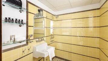 A bathroom with yellow tiled walls, a white sink, and a glass shelf with toiletries.
