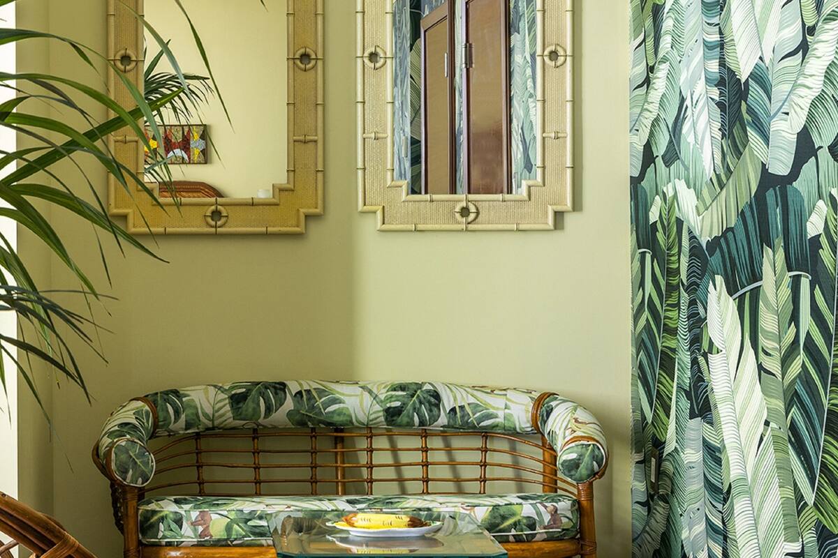 A room with a rattan sofa, two wicker chairs, a small round table, and a large mirror on the wall.