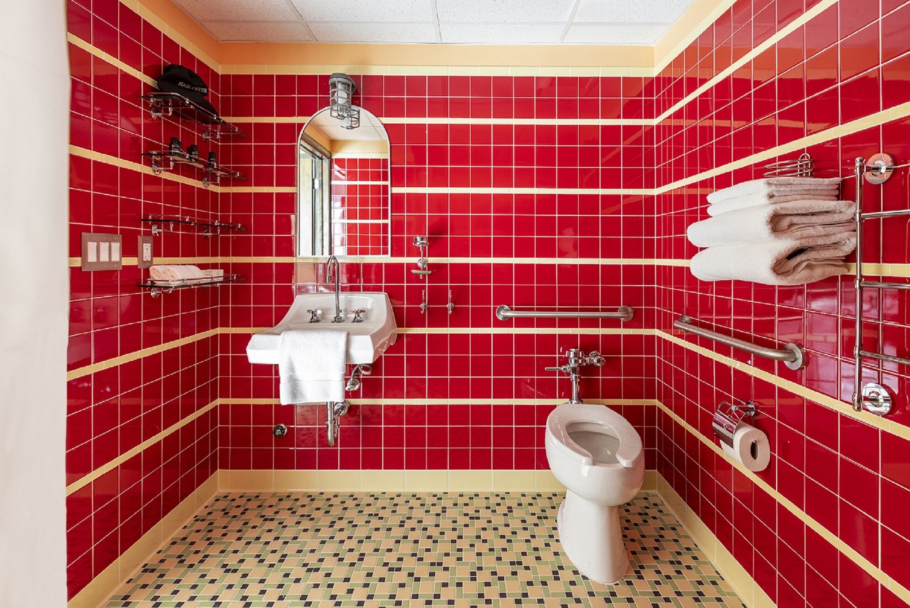 A bathroom with red tiled walls, a white sink, a toilet, and a handrail.