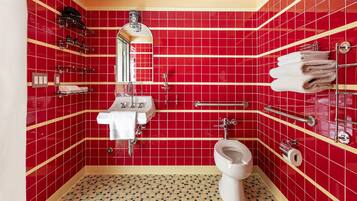 A bathroom with red tiled walls, a white sink, a toilet, and a handrail.