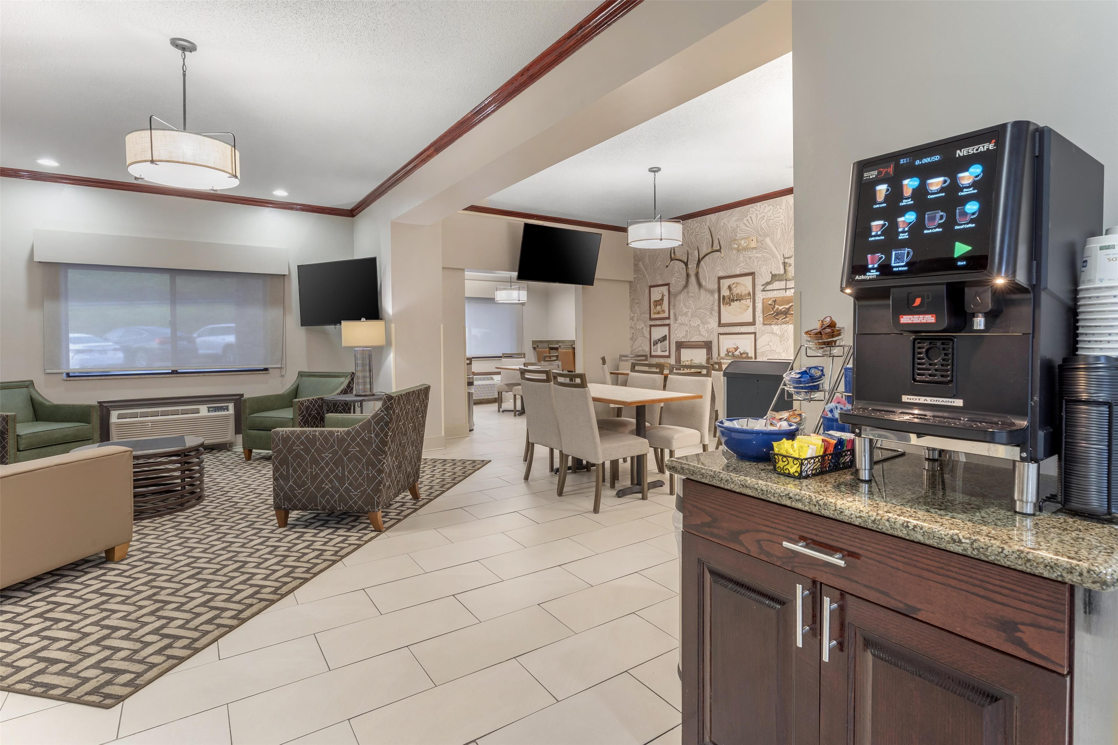 A modern hotel room with a kitchenette, dining area, and a large TV screen.
